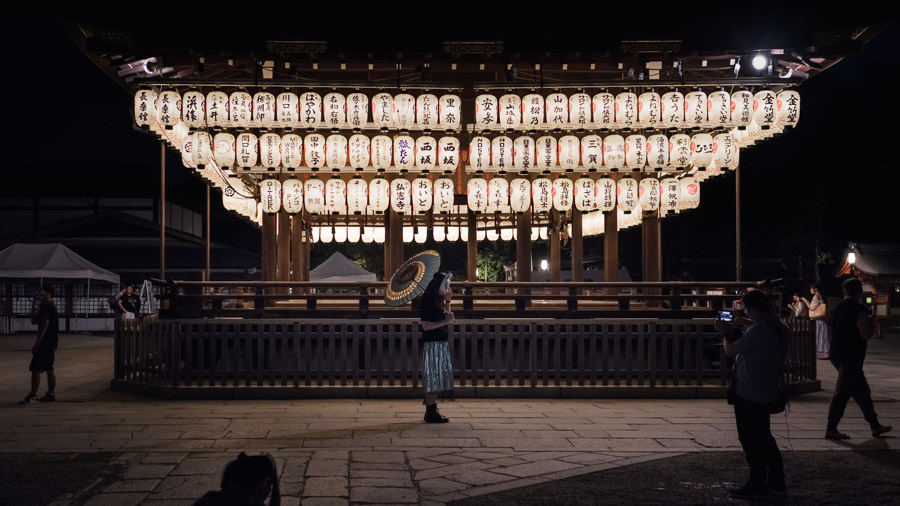 In front of a display of lanterns bearing the names of generous temple donors, a young woman dawns a rabbit mask. In local folklore, the rabbit committed along with other creatures to practice charity on the day of the full moon. Only knowing how to gather grass, the rabbit offered up itself. Recognized for this virtuous action its likeness was said to be drawn upon the moon.