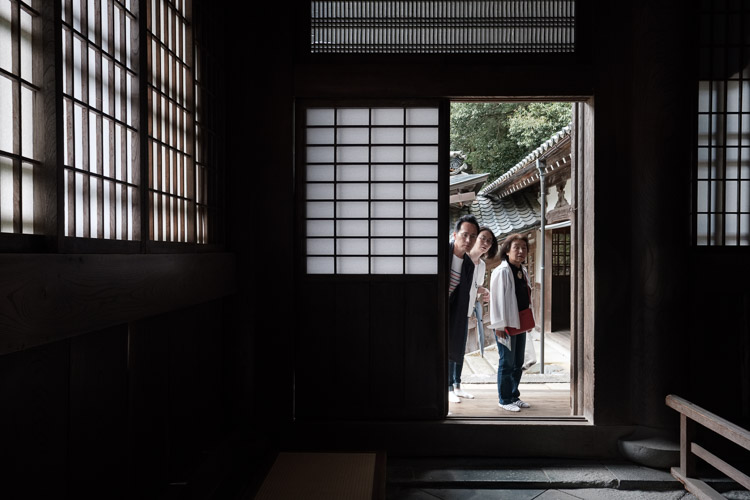 Visitors peek through a door into a practicing Buddhist temple.