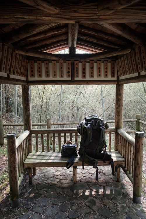 A hiking backpack resting on the bench of a wooden trailside shelter along the Nakasendo trail, bamboo forest beyond