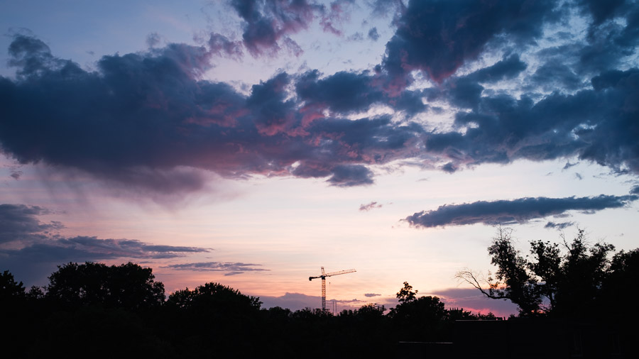 A construction crane silhouetted on the horizon beneath a dramatic pink and blue sunset sky