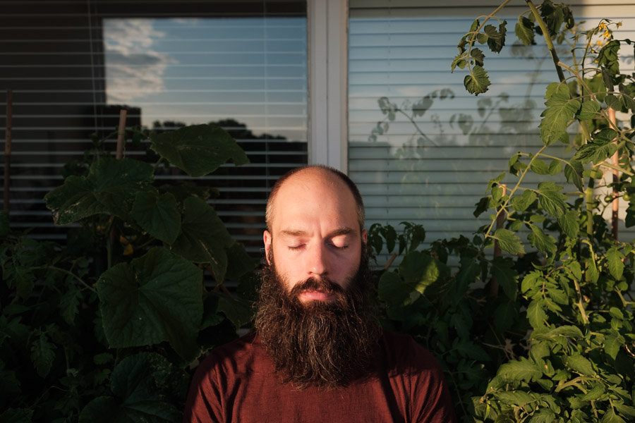 David with eyes closed in golden evening light, framed by tomato and cucumber plants in front of apartment windows