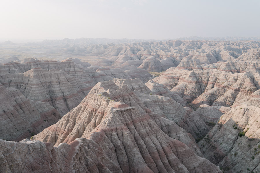 Endless striped ridges and pyramids of the Badlands receding into haze, banded in pink and grey rock
