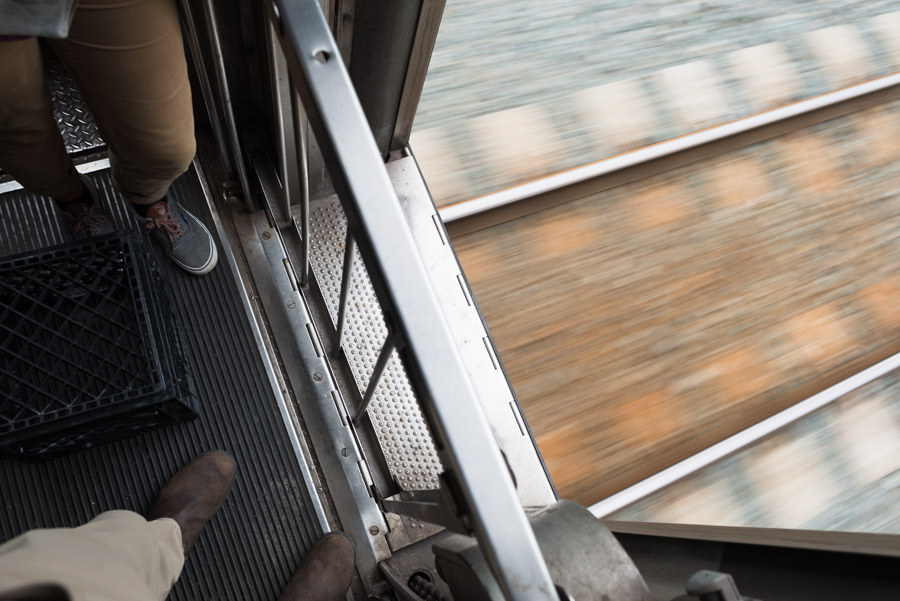 Looking down past passengers' feet through an open train vestibule at tracks blurring by