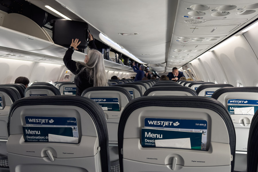 Passengers stow bags in the overhead bins down the aisle of a WestJet cabin