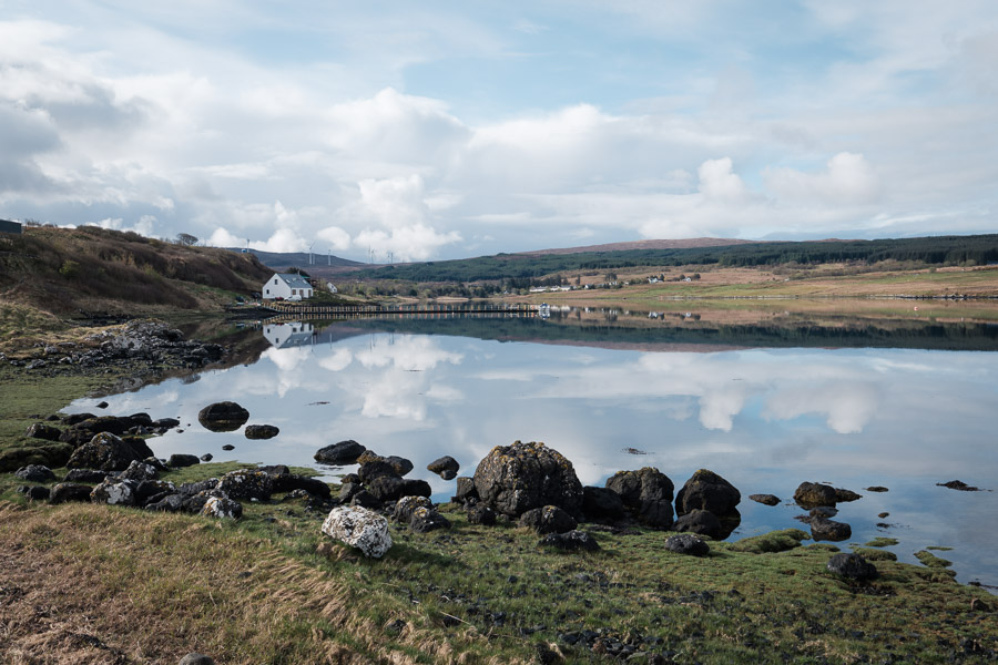 Clouds reflected in a glassy sea loch beside the croft campsite, a white house and green hills along the shore