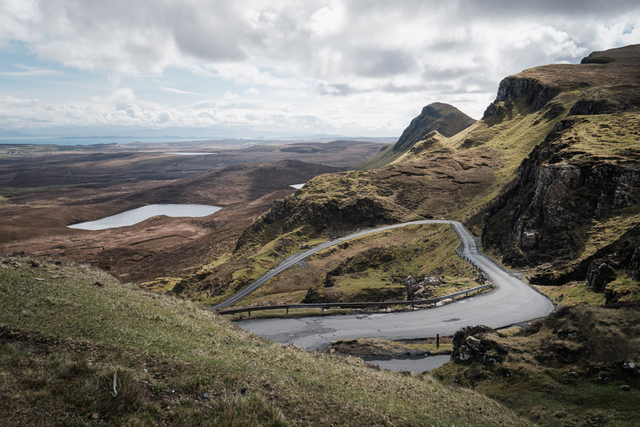 A singletrack road hairpinning through the green cliffs of the Quiraing on the Isle of Skye, lochans and sea in the distance