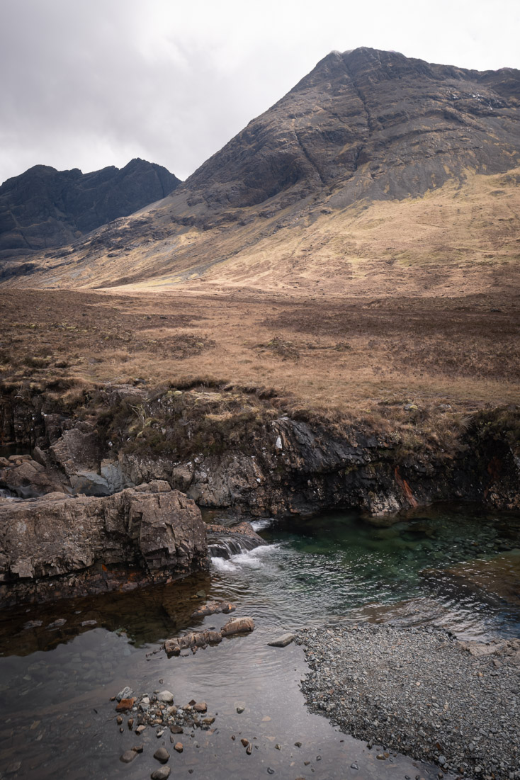 A clear pool and small cascade at the Fairy Pools beneath the dark scree slopes of the Cuillin hills