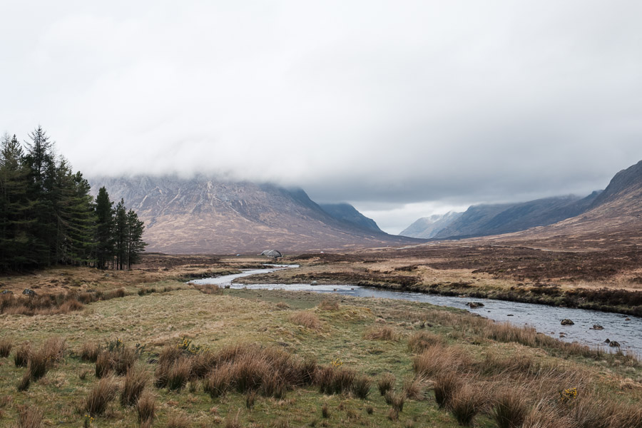A river winding through the Glencoe valley as low cloud swallows the surrounding buttresses