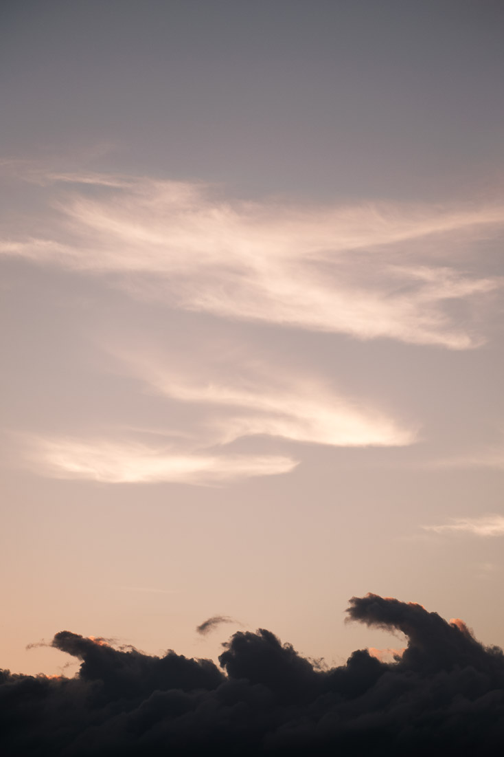 Dark wave-shaped clouds curling like breaking surf along the bottom of a peach dusk sky