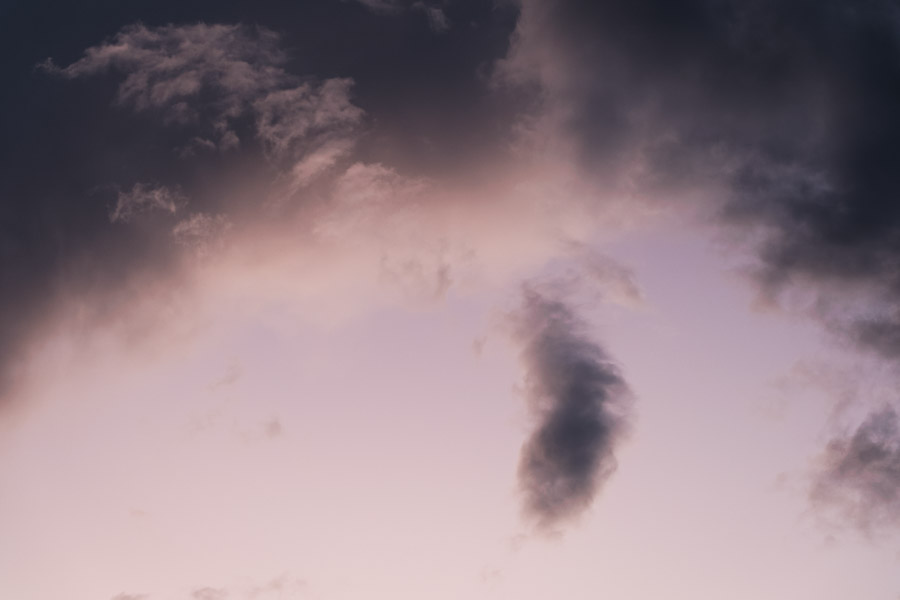 A small dark funnel of cloud hanging in a mauve evening sky between torn storm fragments