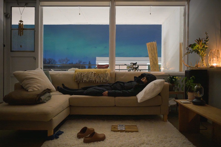 After a few hours gazing at the northern lights from the balcony, a tired apartment dweller naps on the couch in her snowsuit to recharge while the aurora continues to dance across the horizon. Context: The northern lights erupted in such force over Winnipeg that the whole city paused to look up. –photoessay–